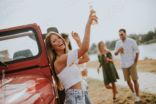 Leinwand Poster Happy young women drinks cider from the bottle by the convertible car