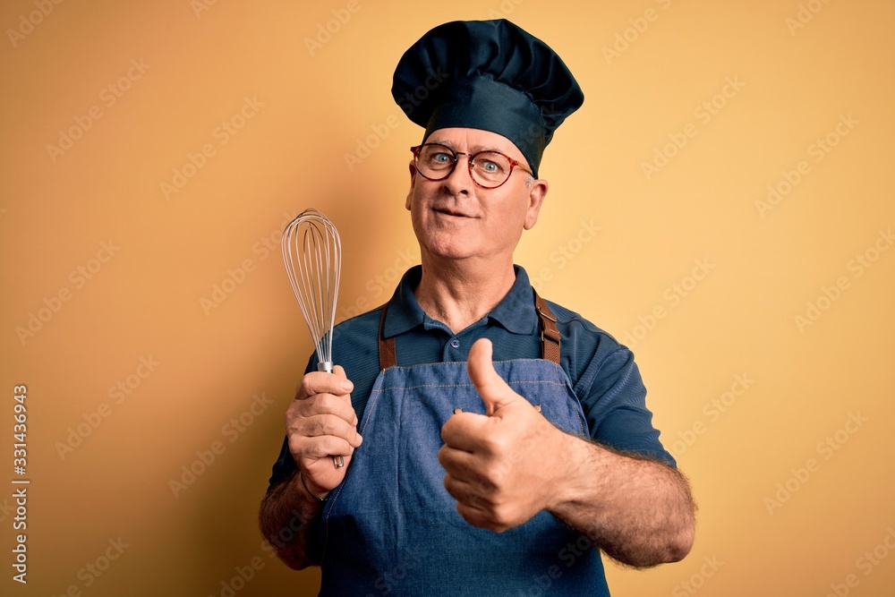 Naklejka premium Middle age hoary cooker man wearing apron and hat holding whisk over yellow background happy with big smile doing ok sign, thumb up with fingers, excellent sign