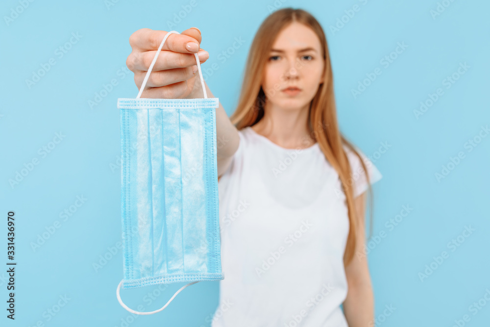 girl holds a hygiene mask against infectious diseases, a coronavirus to prevent infection, blue background girl holds a hygiene mask against infectious diseases, a coronavirus to prevent infection, blue background