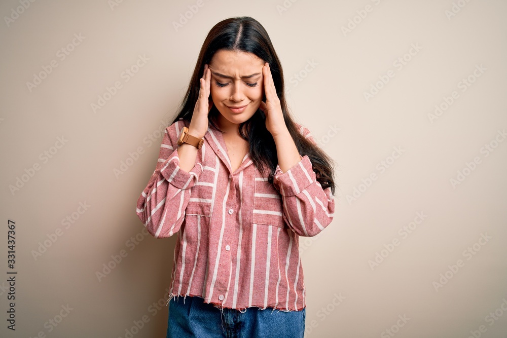 Young brunette woman wearing casual striped shirt over isolated background with hand on head for pain in head because stress. Suffering migraine. Young brunette woman wearing casual striped shirt over isolated background with hand on head for pain in head because stress. Suffering migraine.
