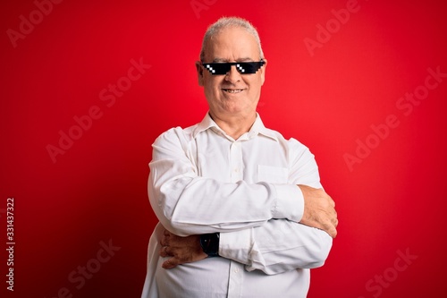 Middle age hoary man wearing funny sunglasses over isolated red background happy face smiling with crossed arms looking at the camera. Positive person.