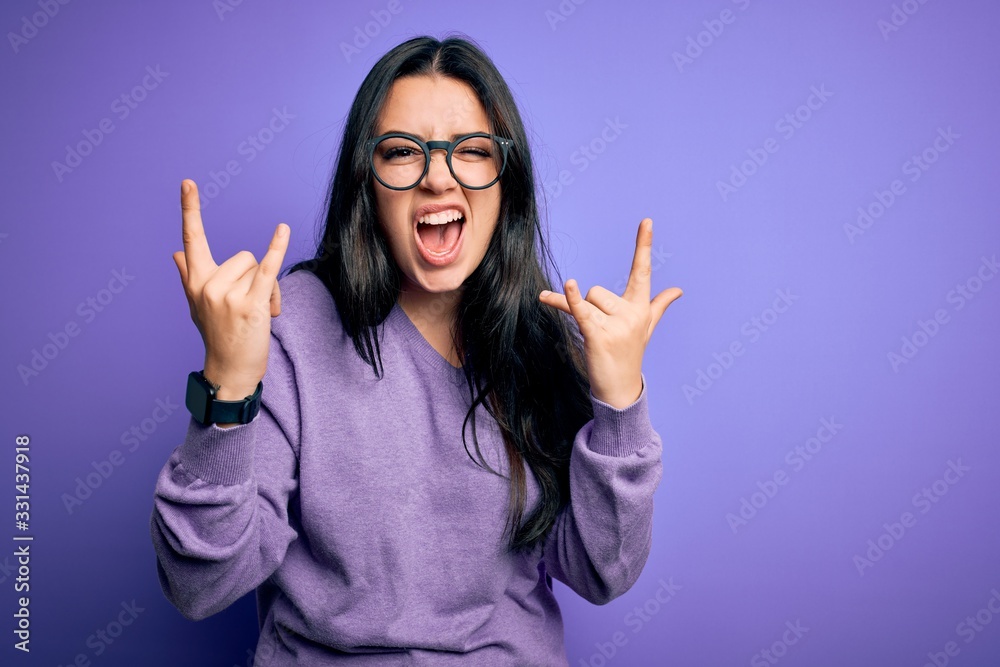 © Krakenimages.com - Young brunette woman wearing glasses over purple isolated background shouting with crazy expression doing rock symbol with hands up. Music star. Heavy concept. © Krakenimages.com - Young brunette woman wearing glasses over purple isolated background shouting with crazy expression doing rock symbol with hands up. Music star. Heavy concept.
