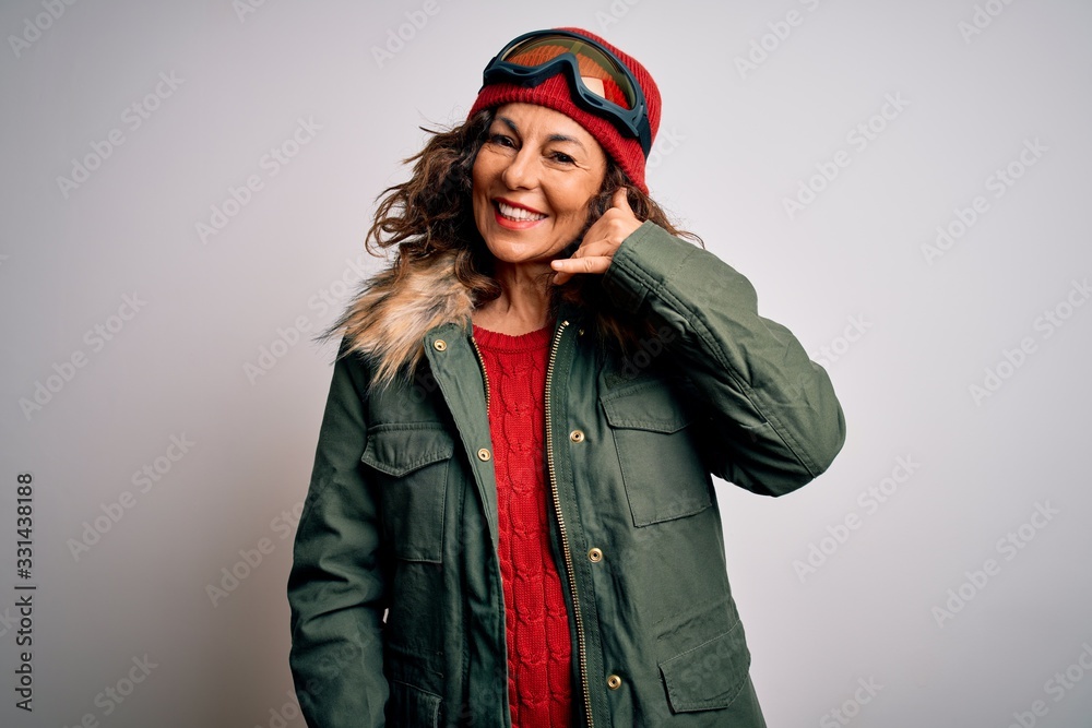 Middle age skier woman wearing snow sportswear and ski goggles over white background smiling doing phone gesture with hand and fingers like talking on the telephone. Communicating concepts.