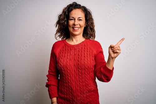 Fotografie Middle age brunette woman wearing casual sweater standing over isolated white background with a big smile on face, pointing with hand finger to the side looking at the camera
