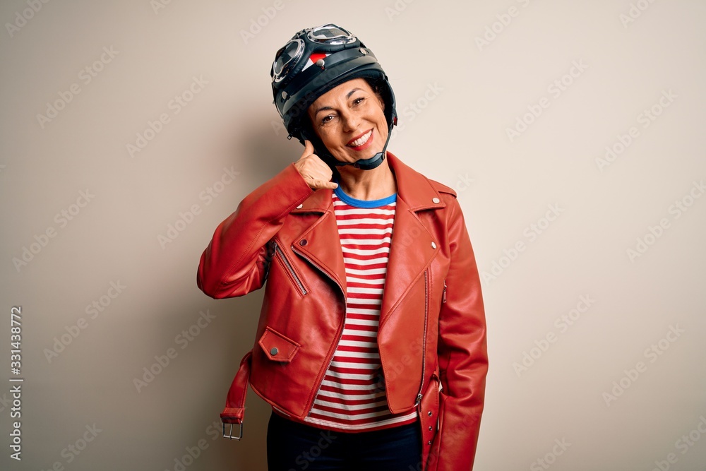 Middle age motorcyclist woman wearing motorcycle helmet and jacket over white background smiling doing phone gesture with hand and fingers like talking on the telephone. Communicating concepts. Middle age motorcyclist woman wearing motorcycle helmet and jacket over white background smiling doing phone gesture with hand and fingers like talking on the telephone. Communicating concepts.