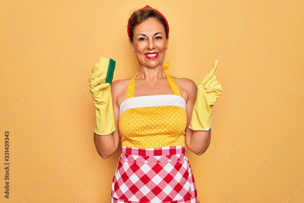 Middle age senior housewife pin up woman wearing 50s style retro dress using cleaner scrub very happy pointing with hand and finger to the side Middle age senior housewife pin up woman wearing 50s style retro dress using cleaner scrub very happy pointing with hand and finger to the side