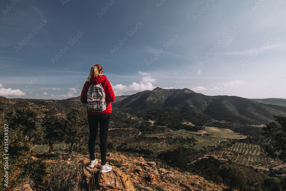 Young woman enjoying view on mountains in sunset, beautiful nature scenery with mountain tops. Girl or woman traveler with backpack alone, woman travelling solo, view from behind, vacation concept Young woman enjoying view on mountains in sunset, beautiful nature scenery with mountain tops. Girl or woman traveler with backpack alone, woman travelling solo, view from behind, vacation concept