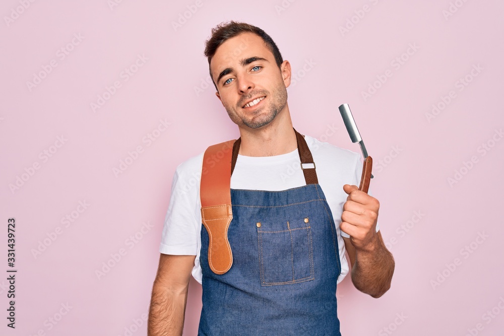 Handsome barber man with blue eyes wearing apron using razor blade over pink background with a happy face standing and smiling with a confident smile showing teeth Handsome barber man with blue eyes wearing apron using razor blade over pink background with a happy face standing and smiling with a confident smile showing teeth