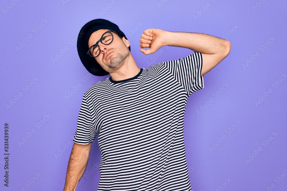 Handsome man with blue eyes wearing striped t-shirt and french beret over purple background stretching back, tired and relaxed, sleepy and yawning for early morning Handsome man with blue eyes wearing striped t-shirt and french beret over purple background stretching back, tired and relaxed, sleepy and yawning for early morning