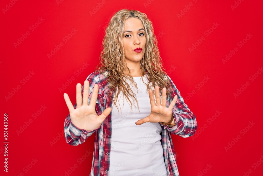 Young beautiful blonde woman wearing casual shirt standing over isolated red background Moving away hands palms showing refusal and denial with afraid and disgusting expression. Stop and forbidden. Young beautiful blonde woman wearing casual shirt standing over isolated red background Moving away hands palms showing refusal and denial with afraid and disgusting expression. Stop and forbidden.