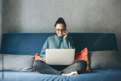 A girl works from home or a student is studying from home or a freelancer. She uses a laptop and a phone.