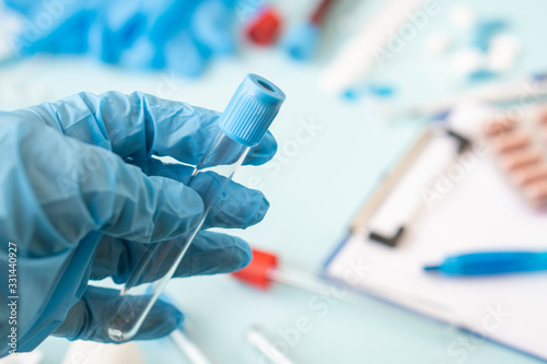 A doctor or nurse holds a test tube to send it to the lab for a blood test. hands of a laboratory assistant with a test tube for taking a blood sample for a virus or flu. Vaccine against the virus .