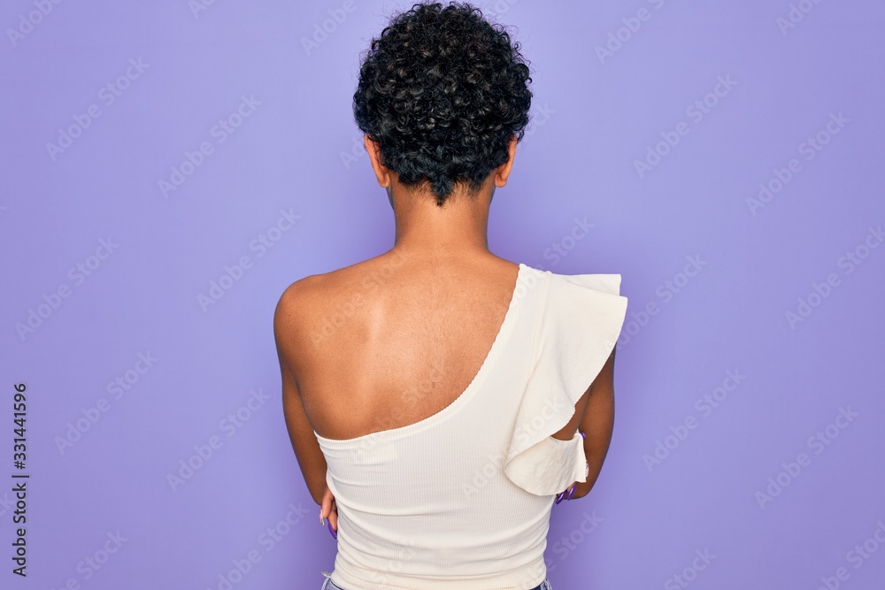 Young beautiful african american afro woman wearing casual t-shirt over purple background standing backwards looking away with crossed arms Young beautiful african american afro woman wearing casual t-shirt over purple background standing backwards looking away with crossed arms