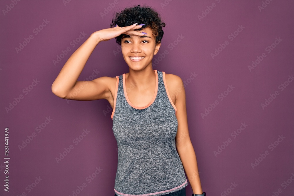 Young beautiful african american afro sportswoman doing exercise wearing sportswear very happy and smiling looking far away with hand over head. Searching concept. Young beautiful african american afro sportswoman doing exercise wearing sportswear very happy and smiling looking far away with hand over head. Searching concept.