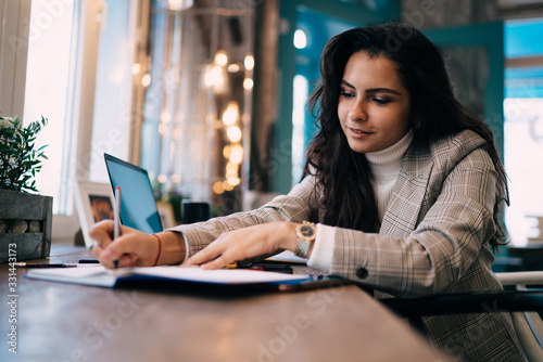 Smiling lady making notes sitting at table with laptop