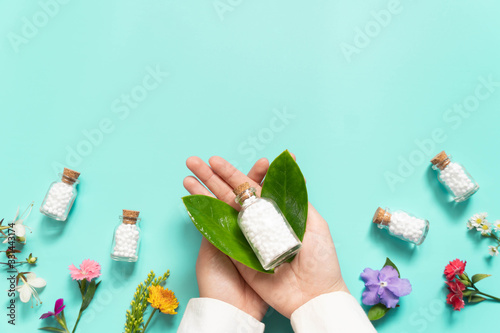 Doctor hands holding homeopathic globules​ bottle with wild flowers​ on green backgound. Homeopathy alternative medicine concept. Flat​ layout. Copy space. photo