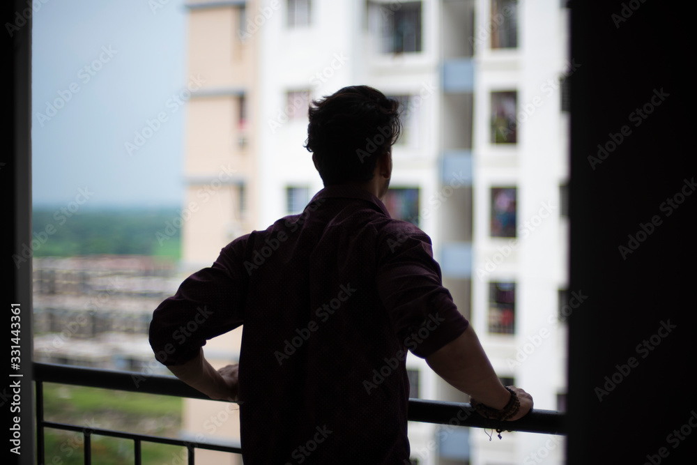 Back portrait of an young and handsome brunette Bengali muscular man in casual shirt and jeans standing on a balcony in white urban background. Indian lifestyle. Back portrait of an young and handsome brunette Bengali muscular man in casual shirt and jeans standing on a balcony in white urban background. Indian lifestyle.