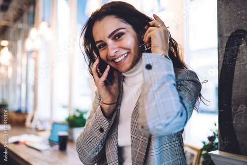 Half length portrait of cheerful millennial female making cellphone conversation for communicate with friend, happy woman with brunette hair and cute smile on face looking at camera while phoning