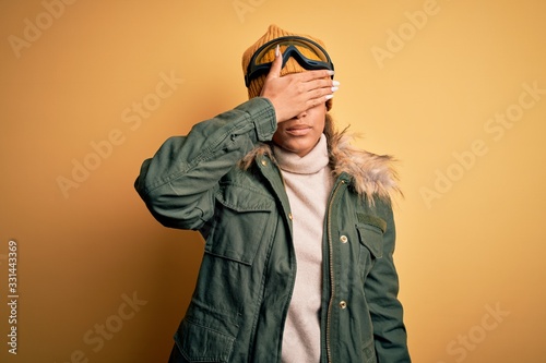 Young african american afro skier girl wearing snow sportswear and ski goggles covering eyes with hand, looking serious and sad. Sightless, hiding and rejection concept © Krakenimages.com