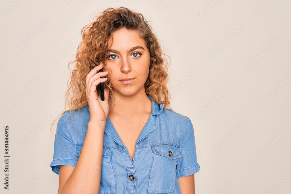 Young beautiful blonde woman with blue eyes having conversation talking on the smartphone with a confident expression on smart face thinking serious Young beautiful blonde woman with blue eyes having conversation talking on the smartphone with a confident expression on smart face thinking serious