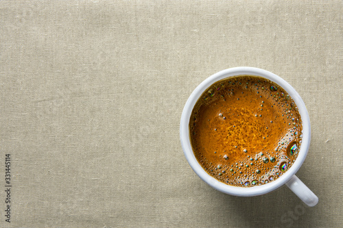 White ceramic cup with freshly brewed hot coffee with crema on linen kitchen table cloth top view. Minimalist style cozy homely atmosphere photo