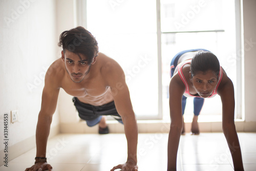 An young Indian Bengali brunette man and dark skinned woman with muscular body doing exercise in a room in white background. Fitness and Indian lifestyle.