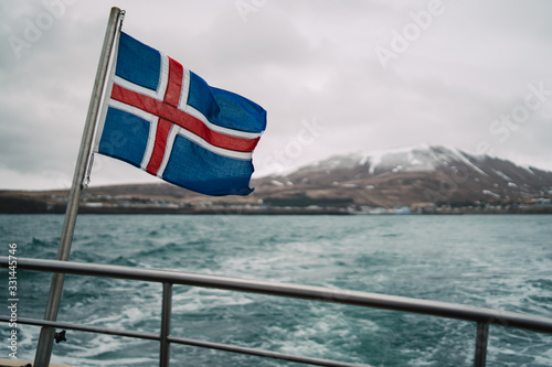 Iceland flag on boat sailing in fjords and view of snowy mountains