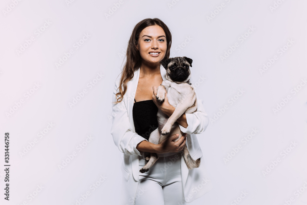 A laughing and smiling auburn haired woman in a white dress, is staring most lovingly at her cute pug, who calmly sits on the hands, gaining her undivided attention. Isolated white background. A laughing and smiling auburn haired woman in a white dress, is staring most lovingly at her cute pug, who calmly sits on the hands, gaining her undivided attention. Isolated white background.