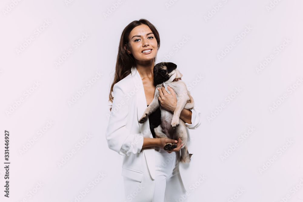 A laughing and smiling auburn haired woman in a white dress, is staring most lovingly at her cute pug, who calmly sits on the hands, gaining her undivided attention. Isolated white background. A laughing and smiling auburn haired woman in a white dress, is staring most lovingly at her cute pug, who calmly sits on the hands, gaining her undivided attention. Isolated white background.