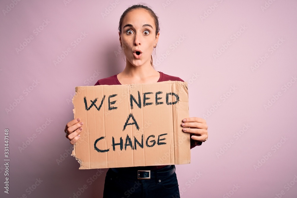 Young beautiful activist woman asking for change protesting holding banner with message scared in shock with a surprise face, afraid and excited with fear expression Young beautiful activist woman asking for change protesting holding banner with message scared in shock with a surprise face, afraid and excited with fear expression