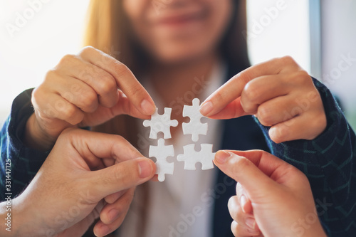 Closeup image of a group of people holding and putting a piece of white jigsaw puzzle together