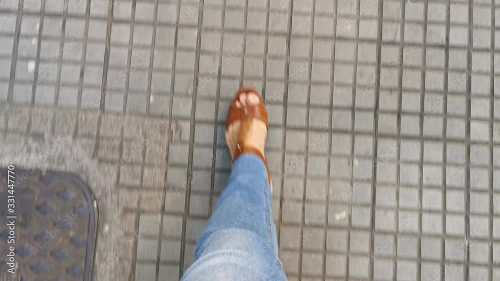 POV. Feet in brown sandals, classic blue jeans, walk on the sidewalk. POV. Feet in brown sandals, classic blue jeans, walk on the sidewalk.