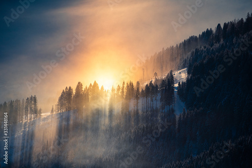 Goldenes Licht mit Sonnenstrahlen durch nebeliges Gebirge mit verschneiten Tannen.  photo