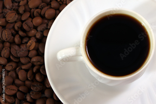 A white cup of coffee and coffee beans on a wooden table.