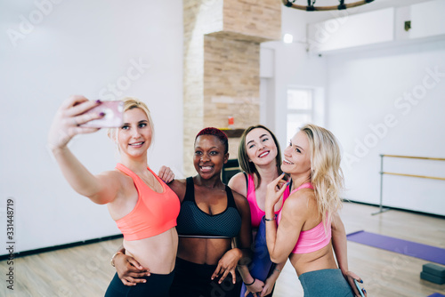 Multiracial smiling embracing sportswomen taking selfie on smartphone