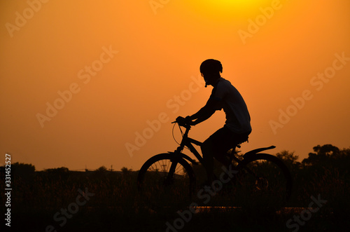 Silhouette men riding bicycles at sunset with orange sky in the countryside