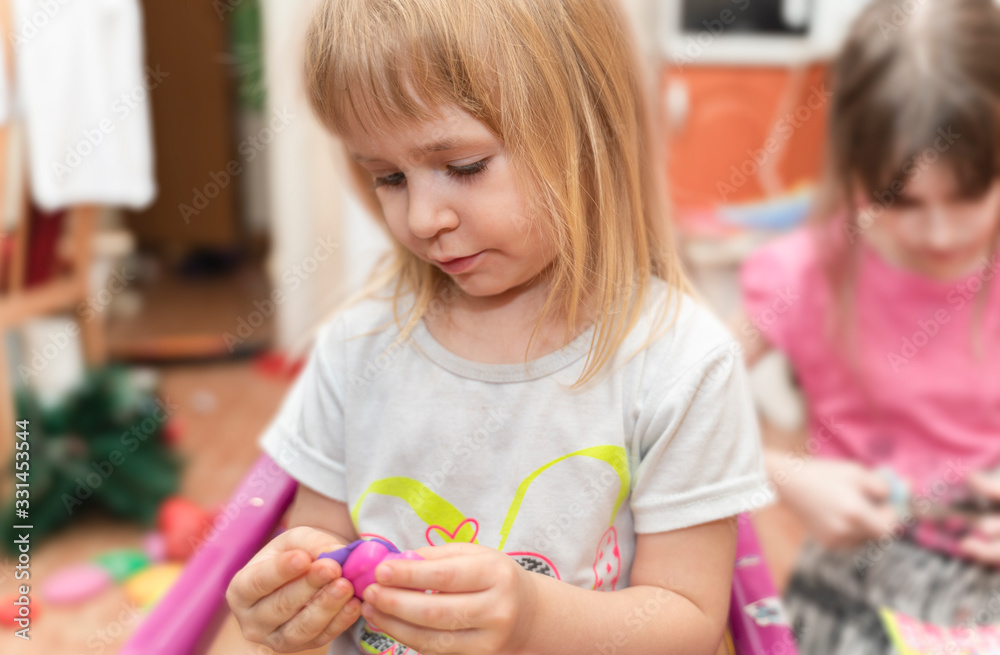 Children at home in living room play with clay. Cute girls enjoy playing with plasticine. Sisters like to spend time together. Children at home in living room play with clay. Cute girls enjoy playing with plasticine. Sisters like to spend time together.