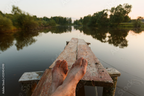 legs of a man resting by the pond in the rays at sunset day