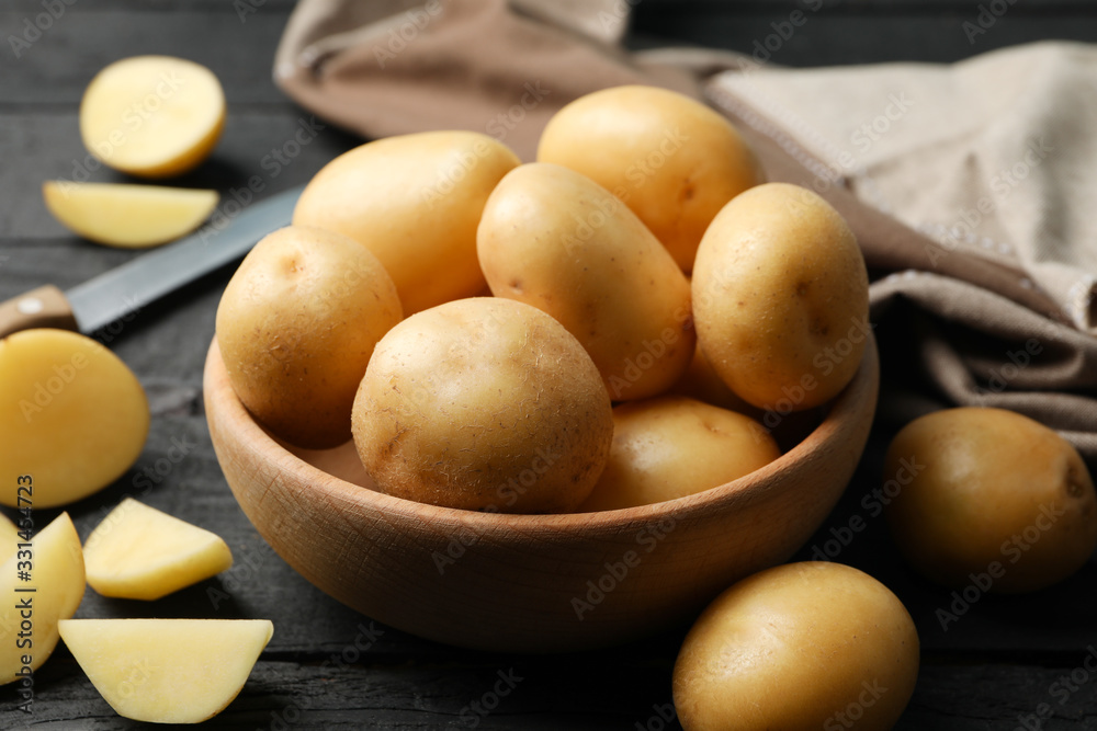 Bowl with young potato, towel and knife on wooden background, close up Bowl with young potato, towel and knife on wooden background, close up