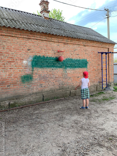 The concept: the game of ball, sports, leisure, child. A boy plays basketball on the street alone against a brick wall.