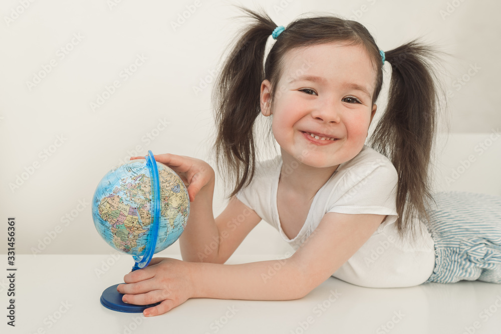 A child examines the globe. Cute girl exploring the planet earth. A child with two ponytails plays with a small globe A child examines the globe. Cute girl exploring the planet earth. A child with two ponytails plays with a small globe