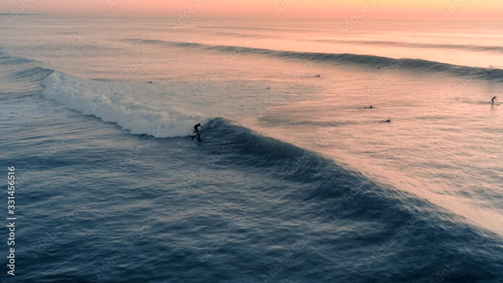Beautiful aerial view of a profesional surfer surfing a perfect wave on a sunset / sunrise. Amazing ocean swell, foam. Top travel destination and extreme sport. Summer time.