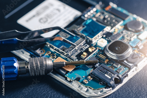 The inside of the smartphone's motherboard and tools lay on the white table. the concept of computer hardware, mobile phone, electronic, repairing, upgrade and technology.