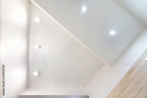 suspended ceiling with led lightspot lamps and drywall construction in empty room in apartment or house. Stretch ceiling white and complex shape. looking up photo