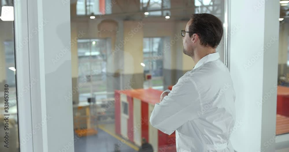 Confident technician in lab coat supervising work of plant through window Confident technician in lab coat supervising work of plant through window