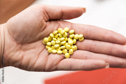 adult's hand close up hold many yellow round medicine, on red and white background