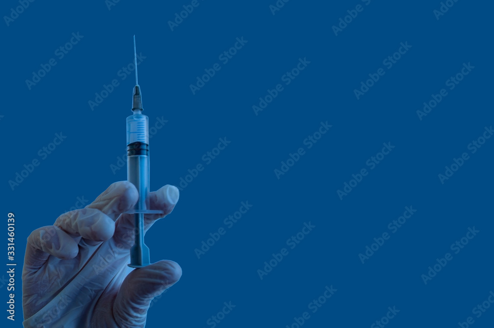 A gloved hand holds a syringe. Medical man using medicine in his hand. Surgeon with an intravenous flu vaccine. Botox injection syringe therapy. isolated on classic blue background A gloved hand holds a syringe. Medical man using medicine in his hand. Surgeon with an intravenous flu vaccine. Botox injection syringe therapy. isolated on classic blue background