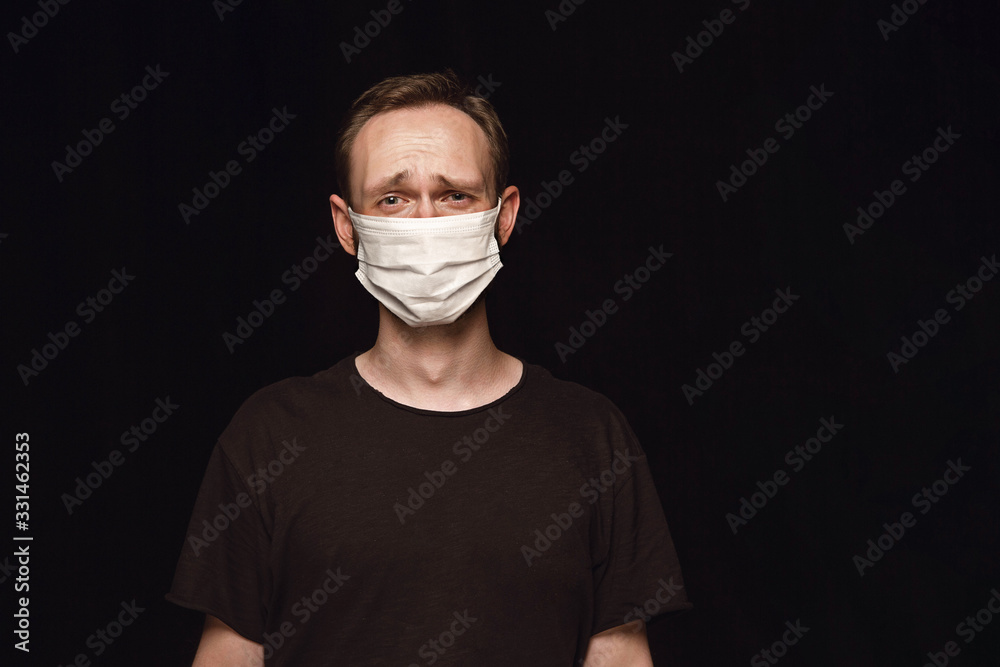 Crying man in protective mask on black background. Prevention against pneumonia, keep on being on quarantine, staying home. Chinese coronavirus treatment. Healthcare, medicine, isolation concept. Crying man in protective mask on black background. Prevention against pneumonia, keep on being on quarantine, staying home. Chinese coronavirus treatment. Healthcare, medicine, isolation concept.