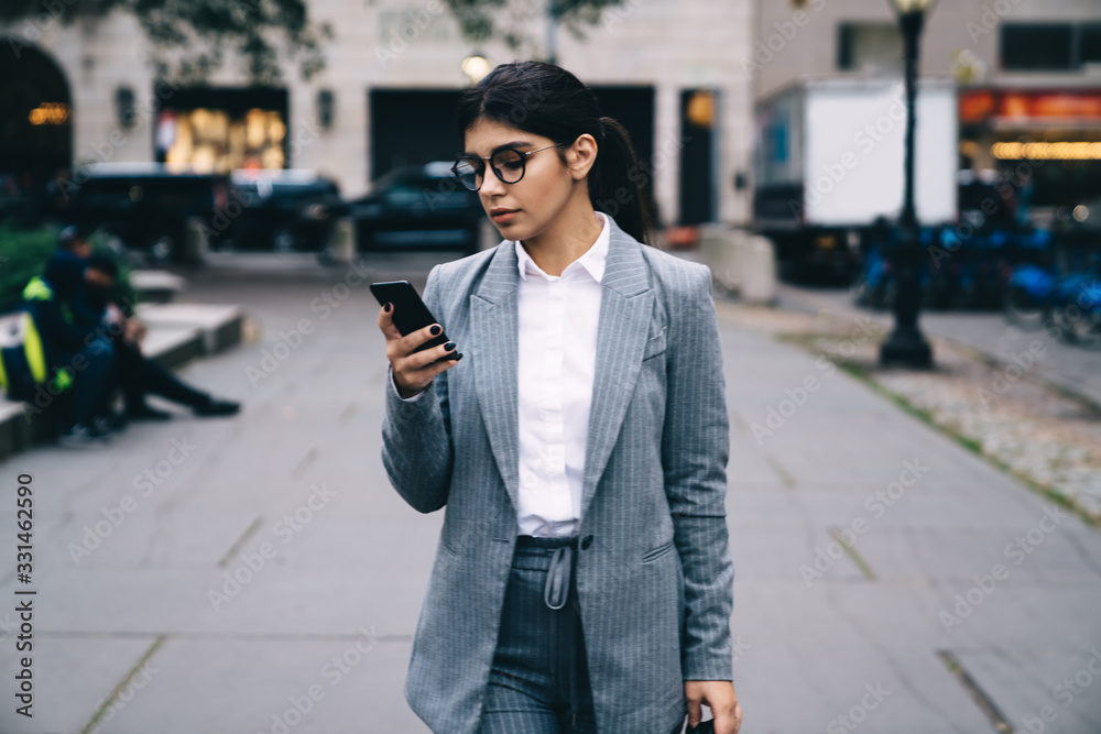Woman CEO in suit reading text message on mobile phone with information from assistant, Hispanic female manager watching financial news on cell smartphone connected to 4g wireless in downtown Woman CEO in suit reading text message on mobile phone with information from assistant, Hispanic female manager watching financial news on cell smartphone connected to 4g wireless in downtown