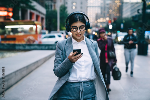 Businesswoman in round glasses walking in downtown and using smartphone